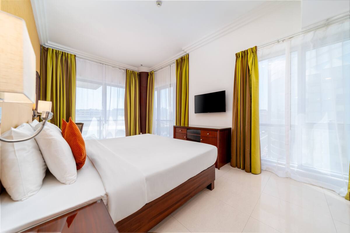 A hotel room with a bed, a TV, a dresser, and curtains.