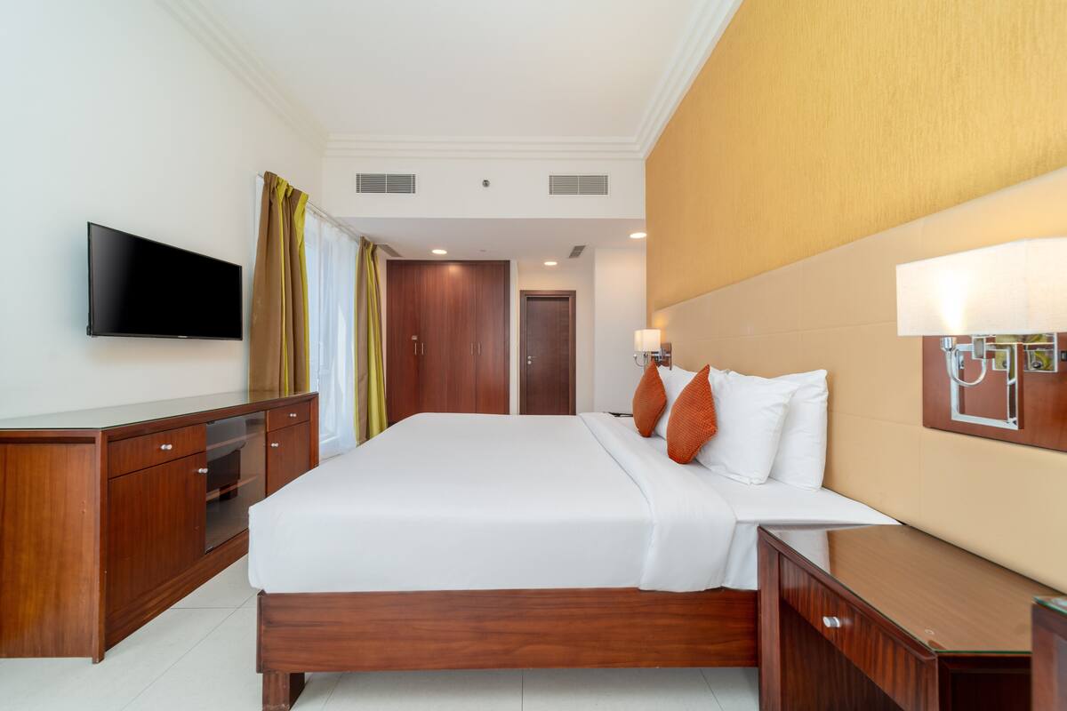 A hotel room with a large bed, wooden furniture, a flat-screen TV, and a bedside lamp.