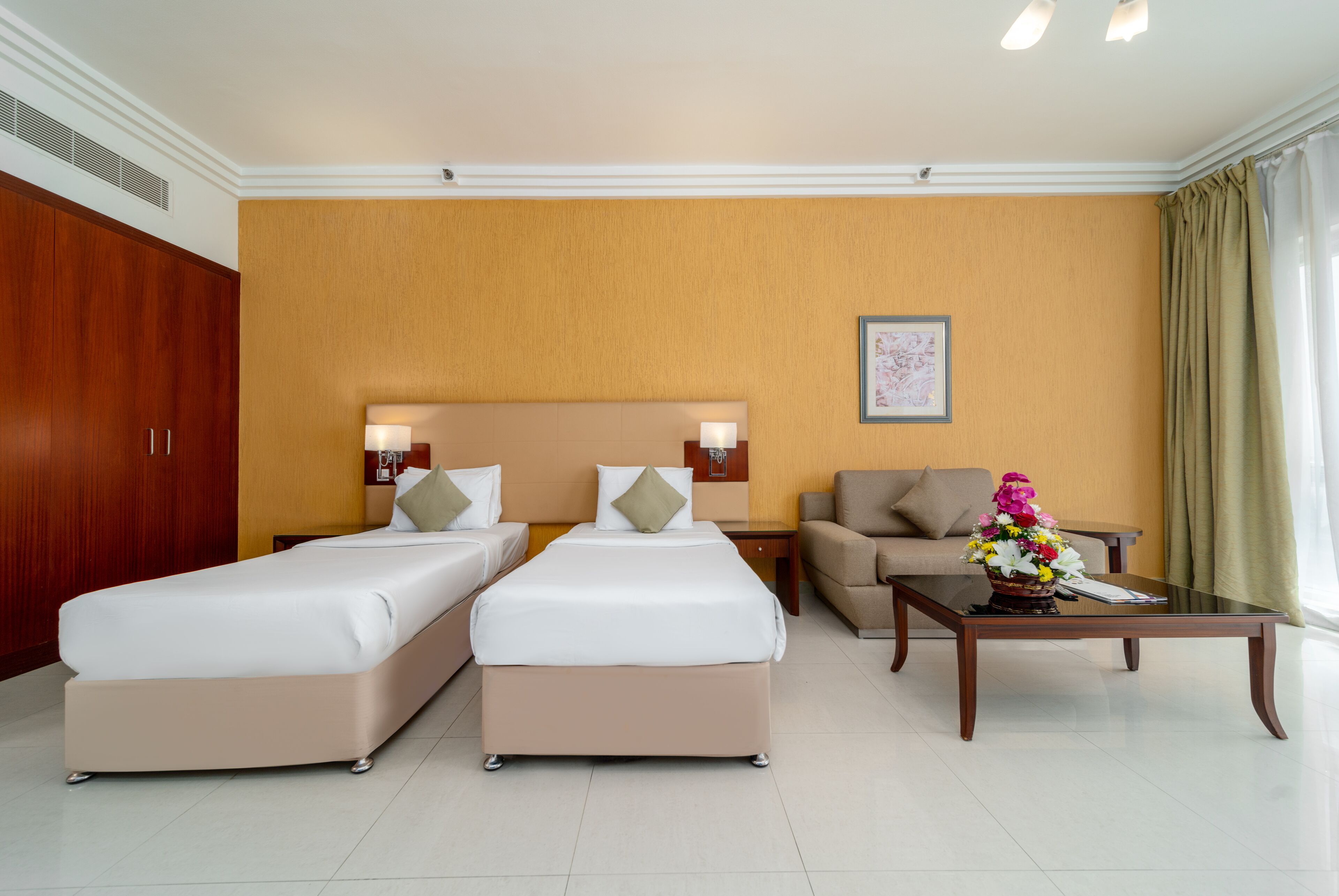 A hotel room with two beds, a sofa, a coffee table with flowers, and a framed picture on the wall.