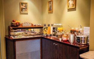 A breakfast bar with various food and drink options, including a fruit bowl, juice dispensers, and jars of spreads.