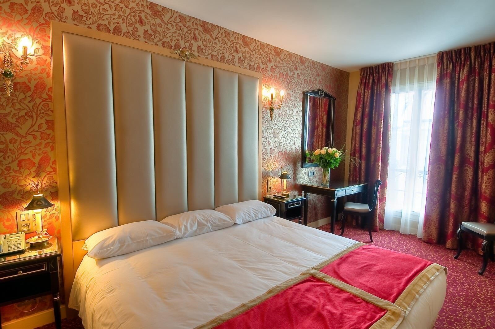 A hotel room with a large bed, a desk, a chair, and a mirror.