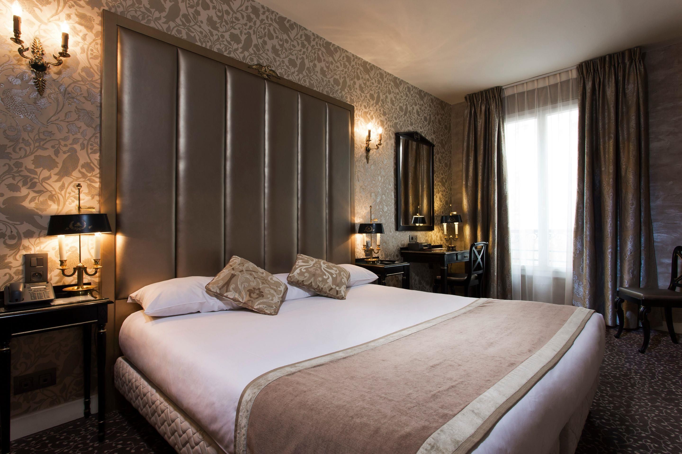 A hotel room with a large bed, two bedside tables, a desk, a chair, a mirror, and a window with curtains.