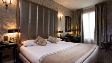 A hotel room with a large bed, two bedside tables, a desk, a chair, a mirror, and a window with curtains.