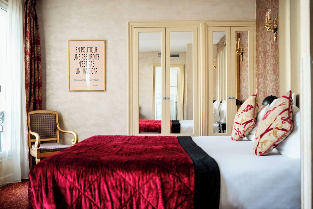 A hotel room with a large bed, a chair, a mirror, and a framed quote on the wall.