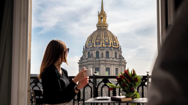Una persona sentada en un balcón con vista a un edificio grande y ornamentado, con una cúpula dorada.