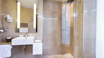 Ein modernes Badezimmer mit einer Duschkabine aus Glas, einem Waschbecken mit Spiegel und einem an der Wand montierten Föhn.