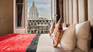Habitación de hotel con una cama, almohadas y vista a un edificio grande a través de una ventana abierta.