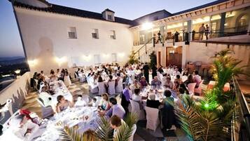 An outdoor dining area with multiple tables and chairs, surrounded by a white building with a balcony.