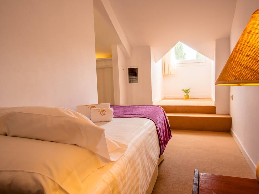 Un dormitorio con cama, ventana, escalera y lámpara.