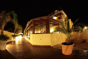 A building with a wooden structure, potted plants, and a paved walkway. - Iride Hotel (San Vito Lo Capo)