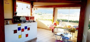 A kitchen with a tiled floor, a counter with a coffee machine, and a view of the countryside through large windows. - Iride Hotel (San Vito Lo Capo)