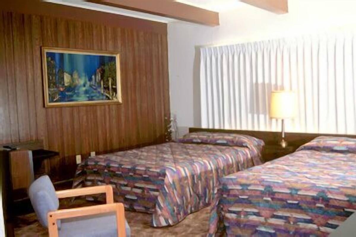 A hotel room with two beds, a painting on the wall, a lamp, and a chair.