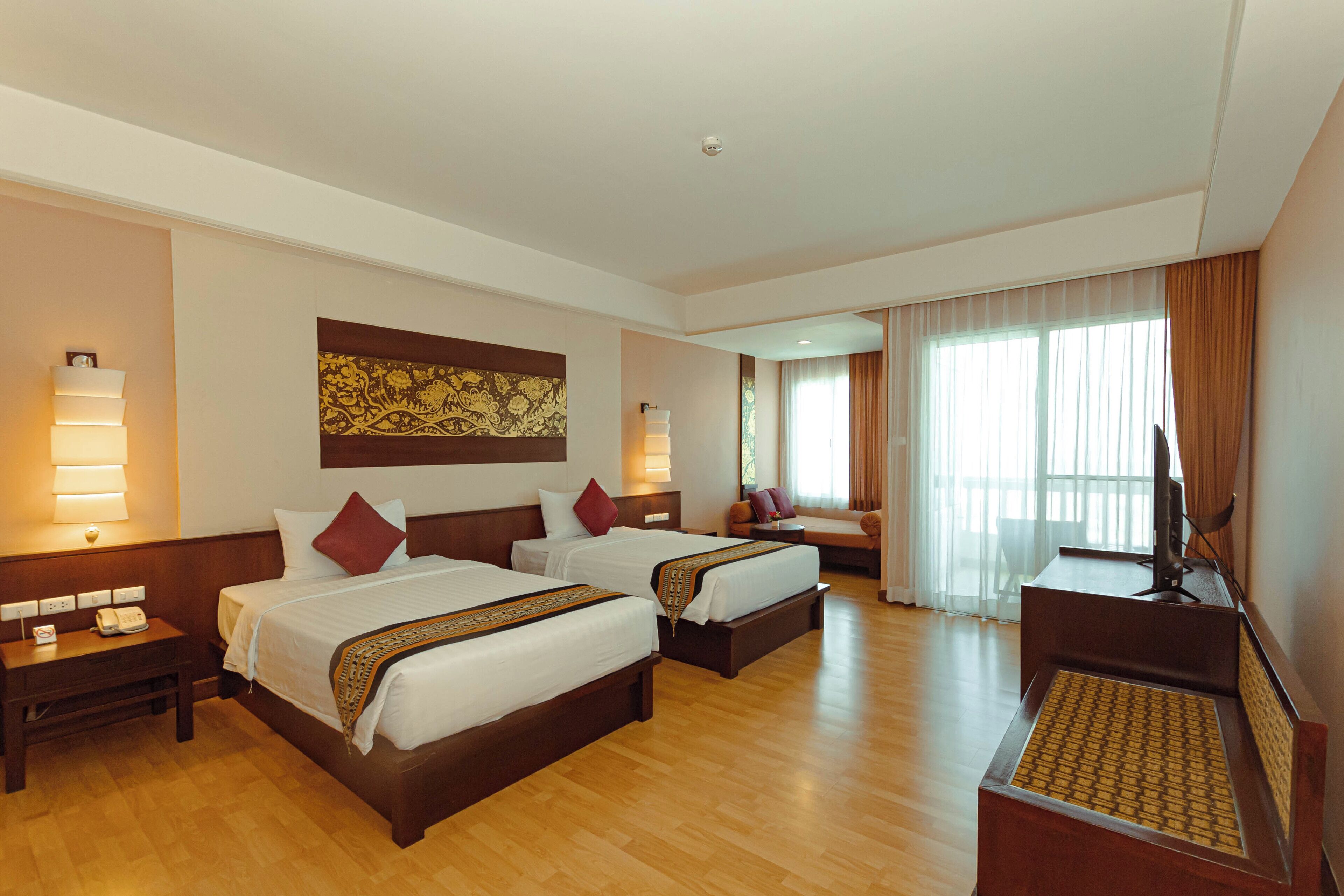 Quarto de hotel com duas camas, uma escrivaninha, televisão e uma janela grande com cortinas.