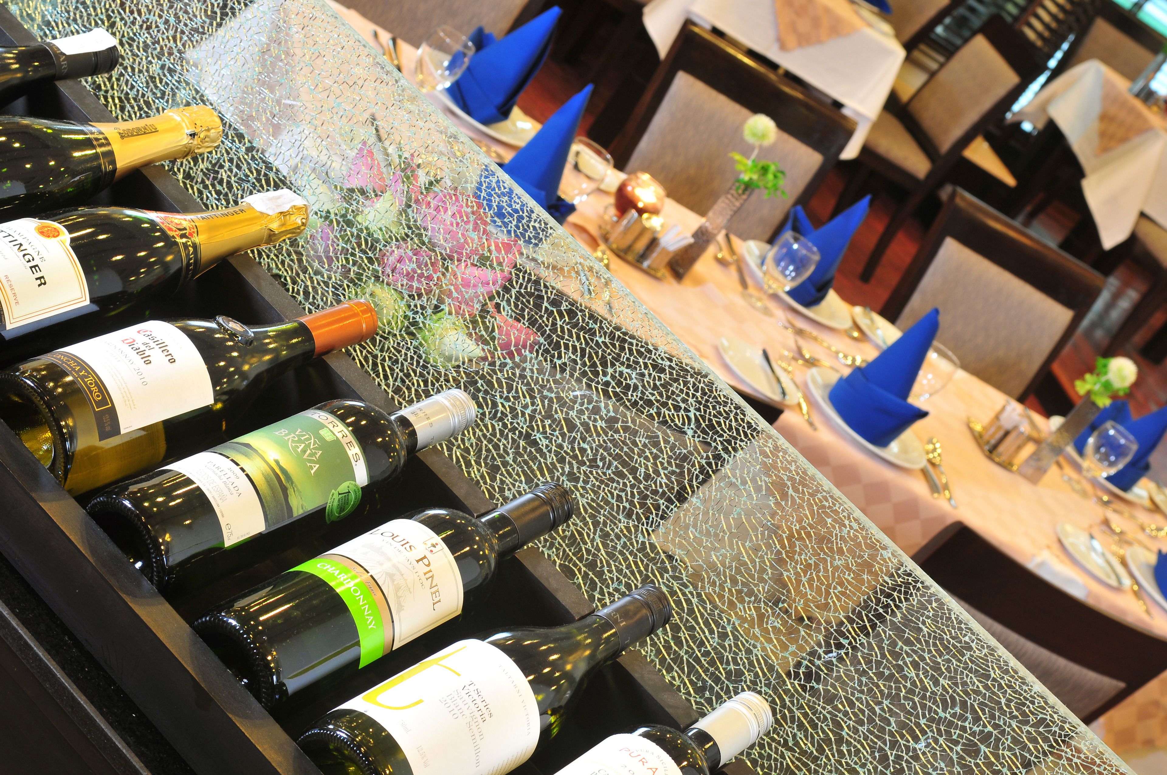 Uma mesa com garrafas de vinho e copos, em um restaurante com guardanapos azuis e um centro de mesa decorativo.