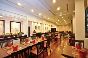 A spacious restaurant with multiple dining tables and chairs, a buffet area with food displays, and a modern interior design. - Tara Angkor Hotel (Siem Reap)