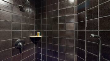 Un baño con paredes de azulejos oscuros, un cabezal de ducha, un inodoro y un pasamanos.