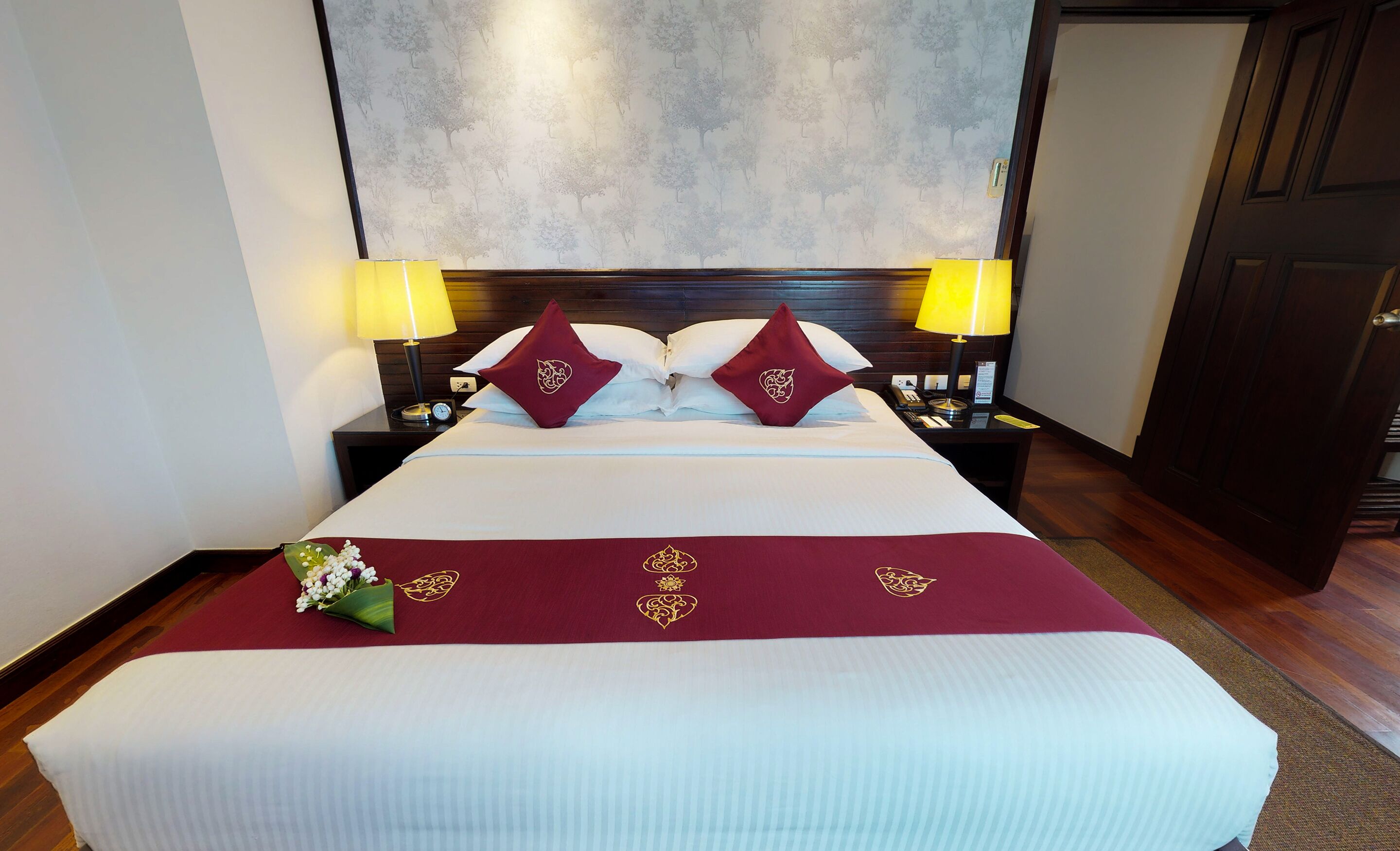 Une chambre d’hôtel avec un grand lit, deux lampes de chevet, une table de nuit et un mur décoré d’un motif représentant un arbre.