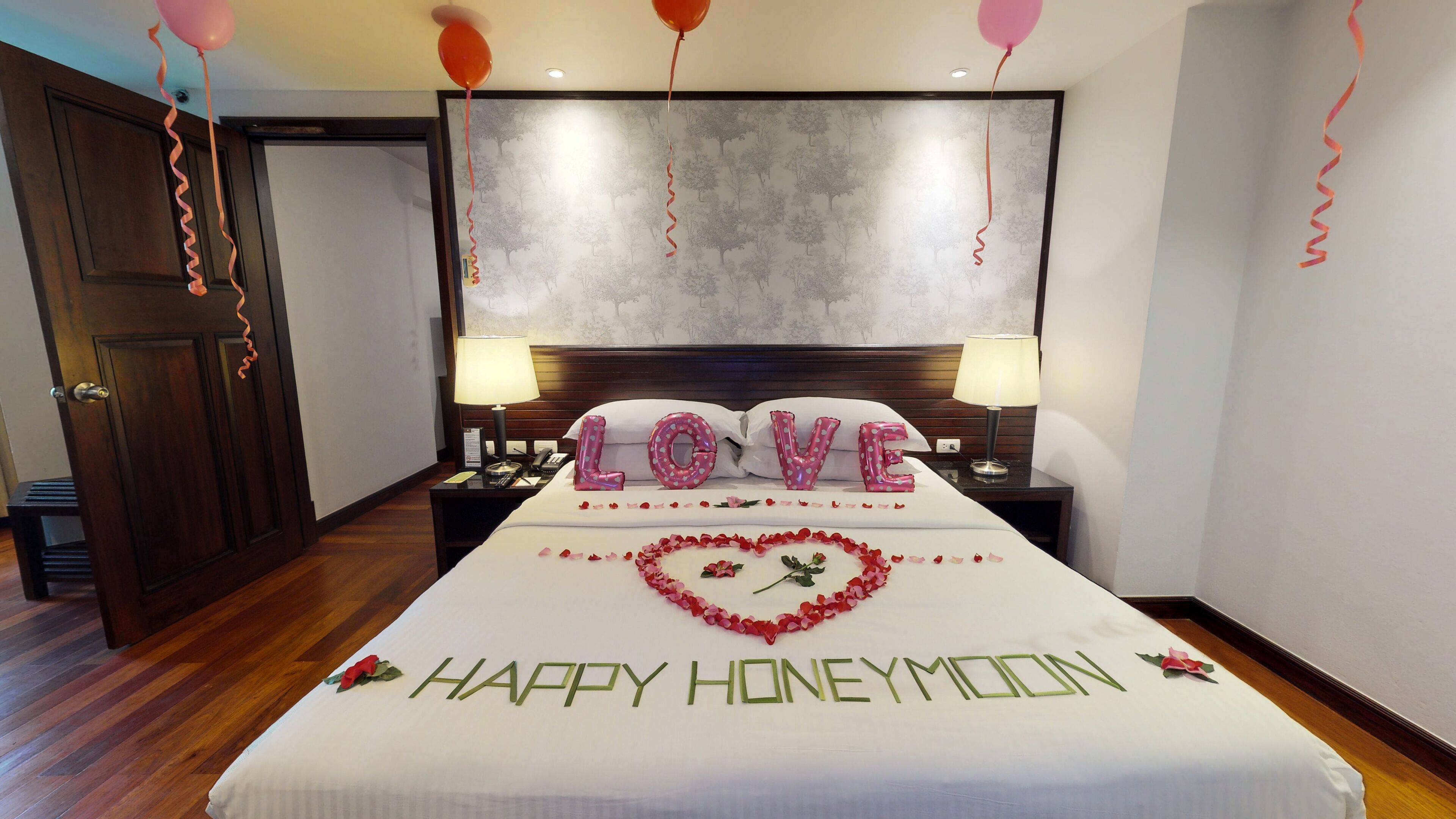 Habitación de hotel con cama, dos lámparas de noche, una mesita de noche y una pared decorada con un diseño de árbol.