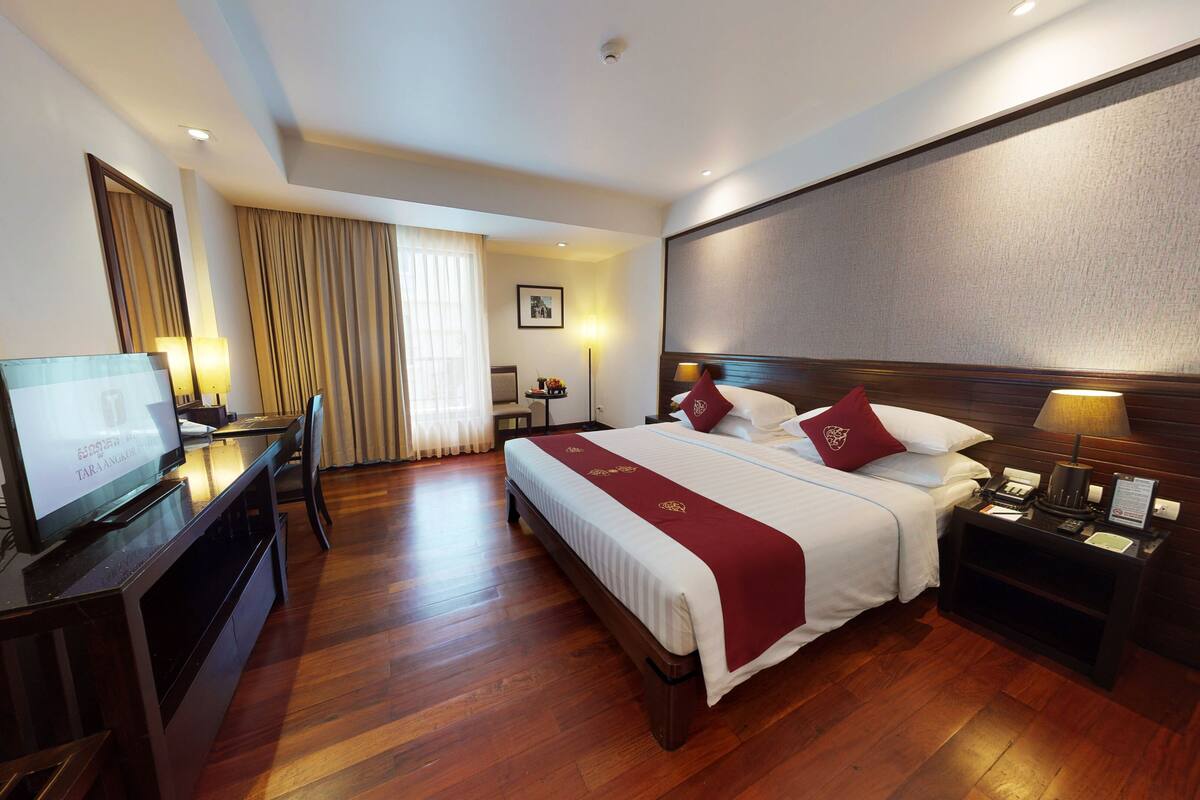 Una habitación de hotel con cama, mesita de noche, lámpara, escritorio con computadora y una silla.