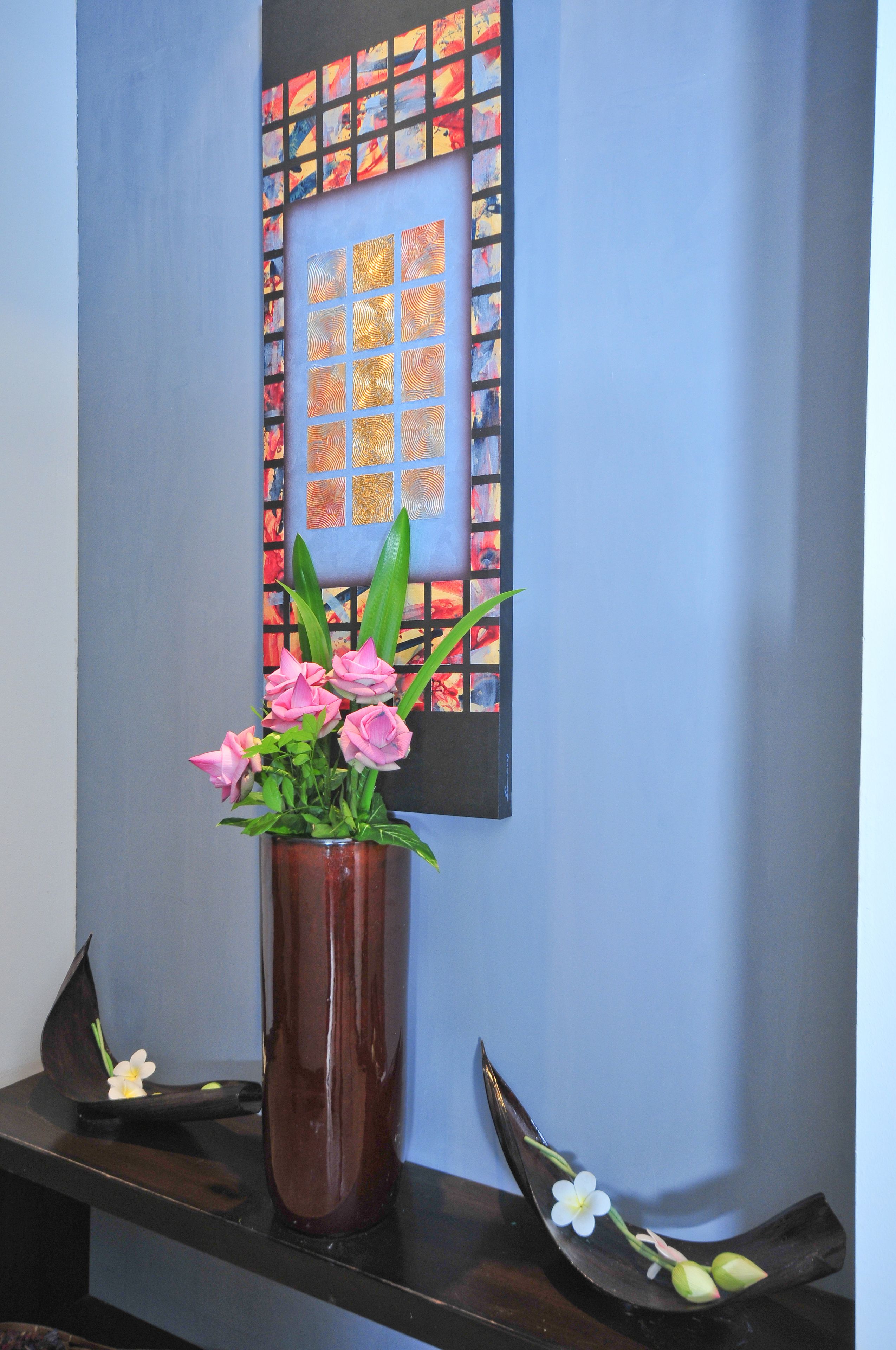 A room with a dark brown vase containing pink flowers and green leaves on a black surface.