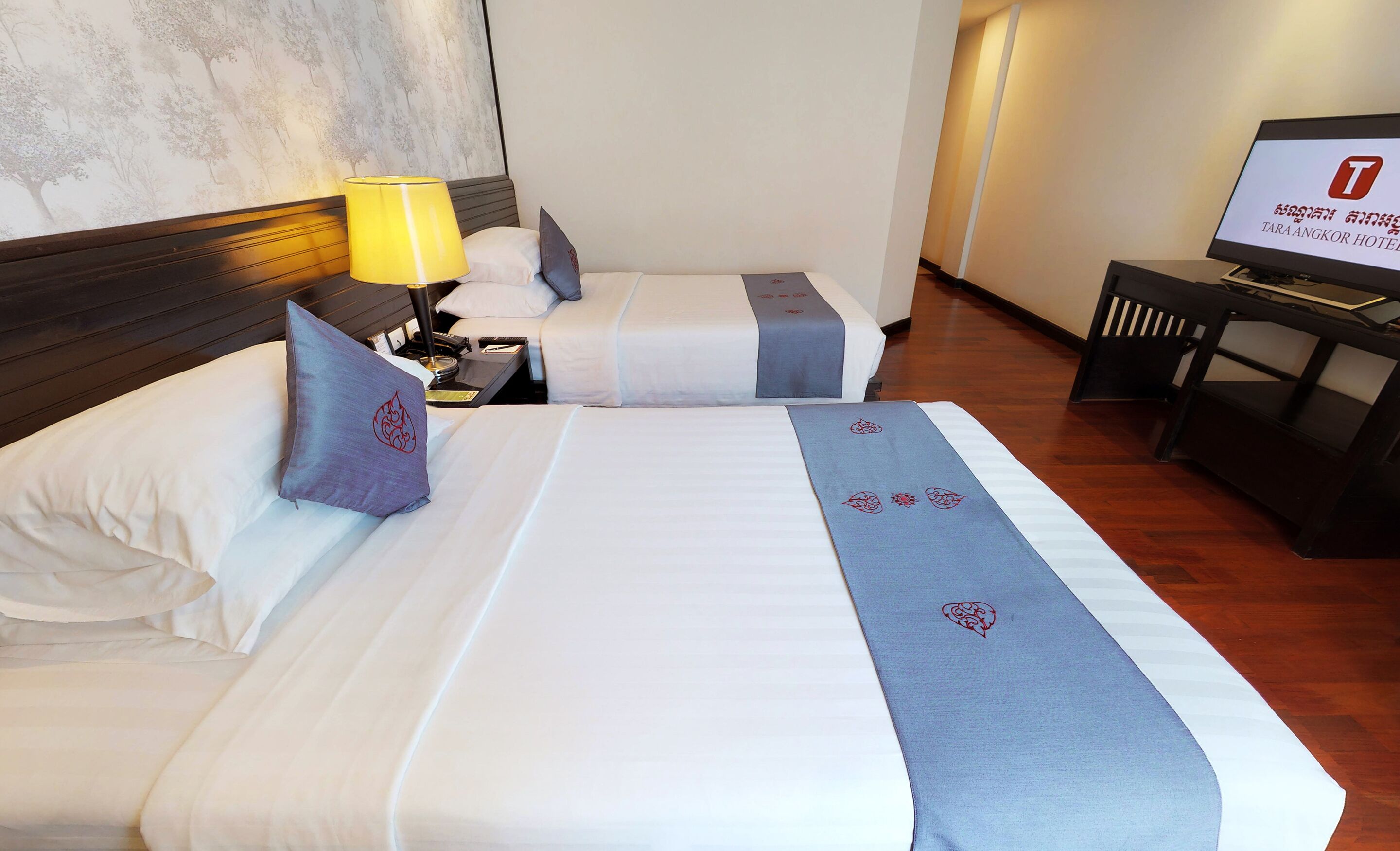 A hotel room with two beds, a TV, and a wooden floor.