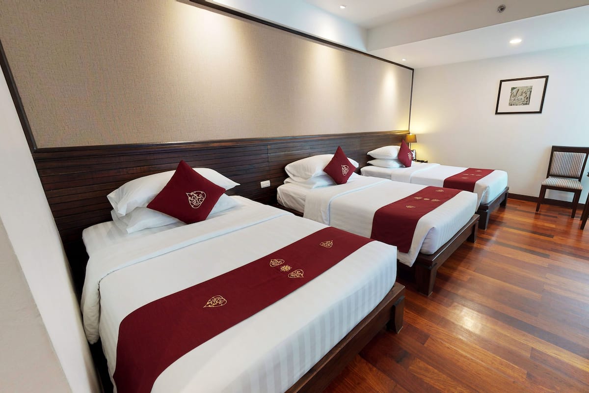 Habitación de hotel con tres camas, cada una con cubrecama rojo y almohadas a juego. La habitación tiene piso de madera y un ventanal grande.