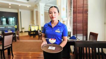 A hotel staff member holding a tray with a dessert. The setting appears to be a dining area with tables and chairs.