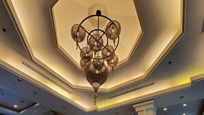 A hotel lobby with a large chandelier, a reception desk, framed pictures on the wall, and a staircase. - Tara Angkor Hotel (Siem Reap)
