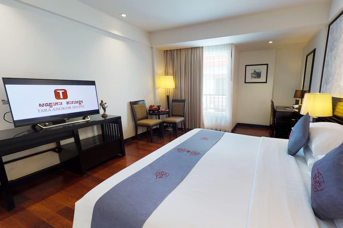 Habitación de hotel con cama, escritorio, silla, televisor y ventana con cortinas.
