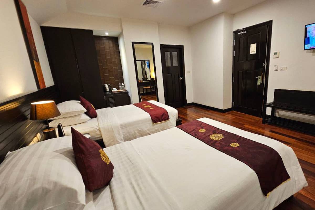 Habitación de hotel con dos camas, un escritorio, una banca, un televisor y un espejo.