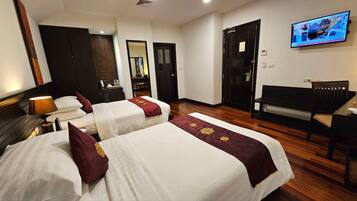 A hotel room with two beds, a desk, a bench, a TV, and a mirror.