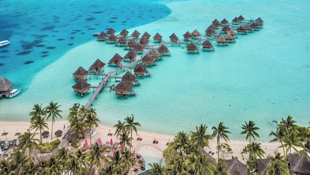 Eine Anordnung von Strandbungalows über dem Wasser, mit Strand und Palmen.