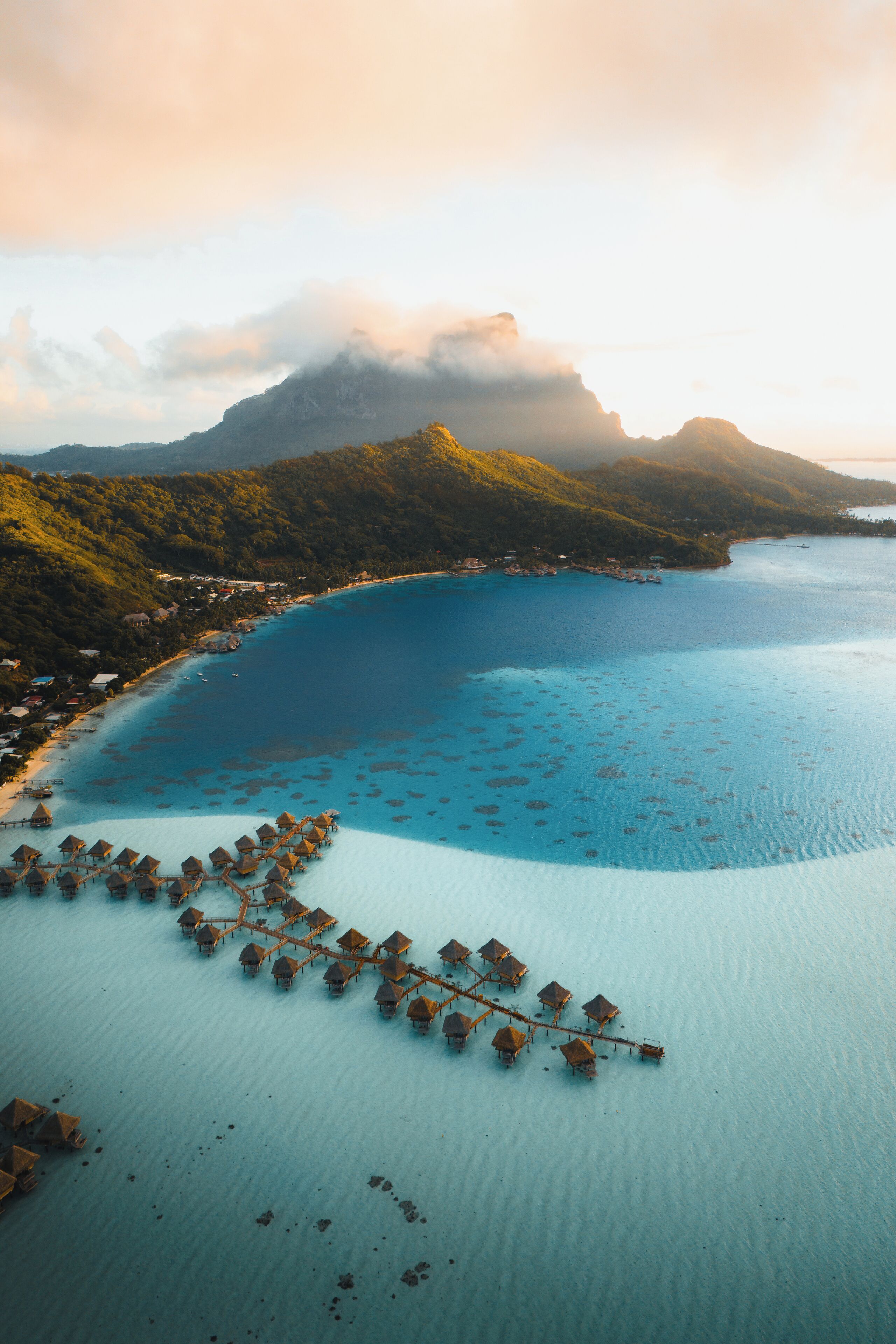 An aerial view of a coastal area with overwater bungalows and a clear blue sea.