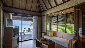 Ein Zimmer mit Holzboden, einer Couch, einem Couchtisch, einem Fernseher und Blick aufs Meer.
