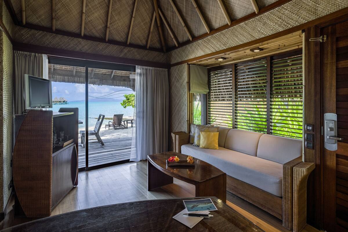 Ein Zimmer mit Holzboden, einer Couch, einem Couchtisch, einem Fernseher und Blick aufs Meer.