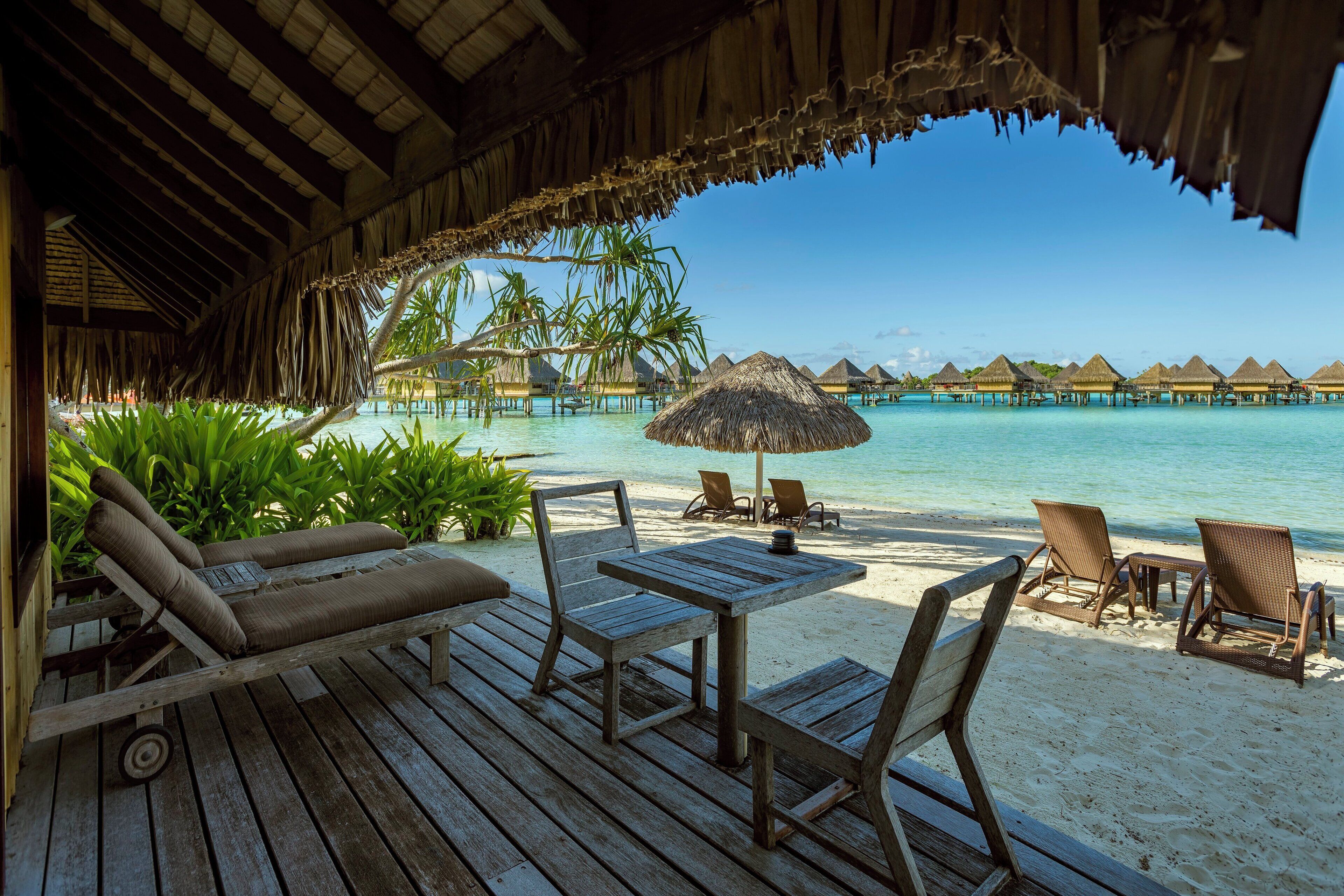 An overwater bungalow with a wooden deck, lounge chairs, and a table.