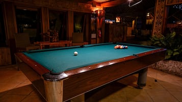 A pool table with a wooden frame and a green felt surface, surrounded by wooden walls and a tiled floor.