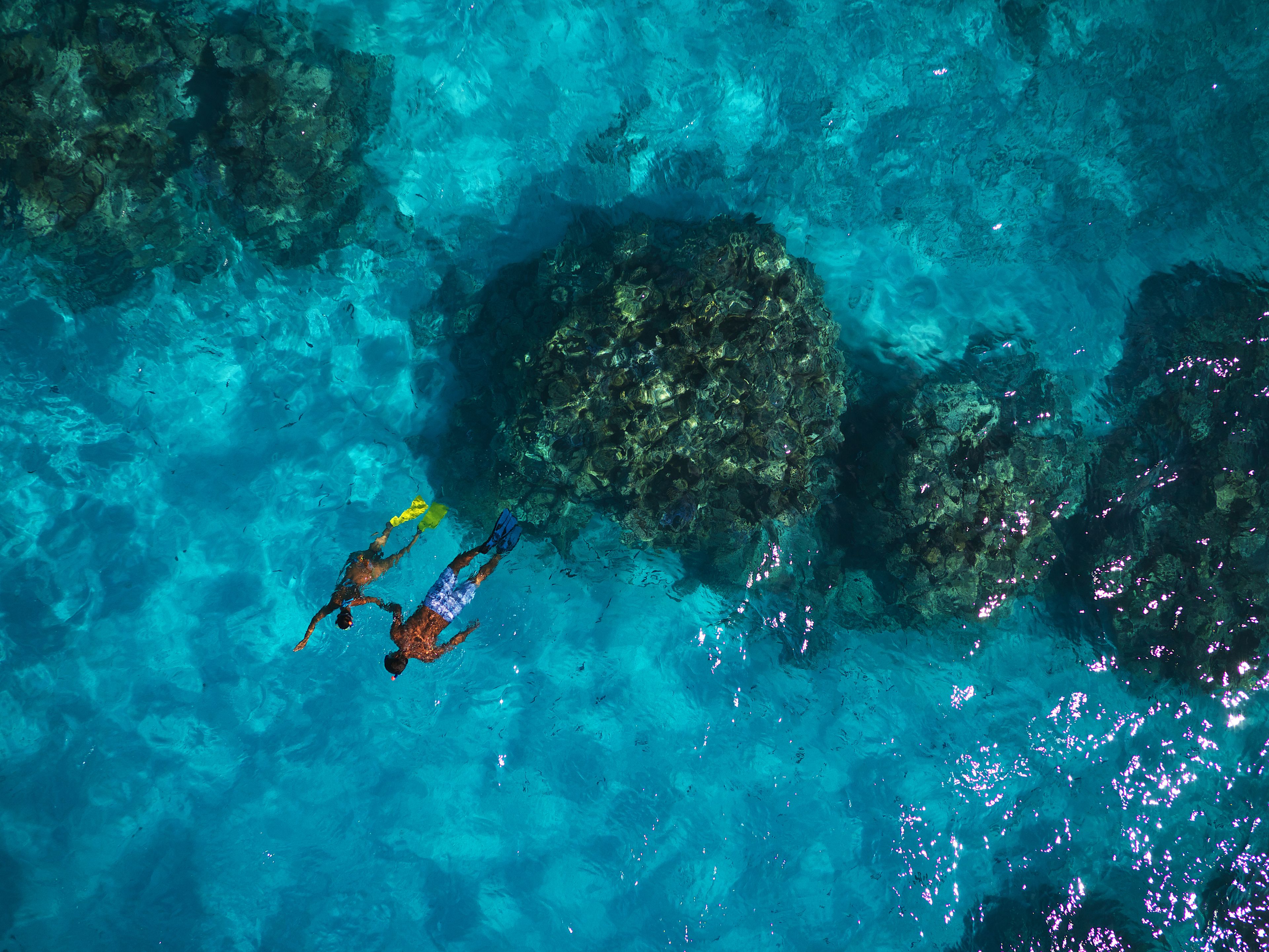 Vue sous-marine d’une mer d’un bleu limpide, avec deux plongeurs et des formations rocheuses.