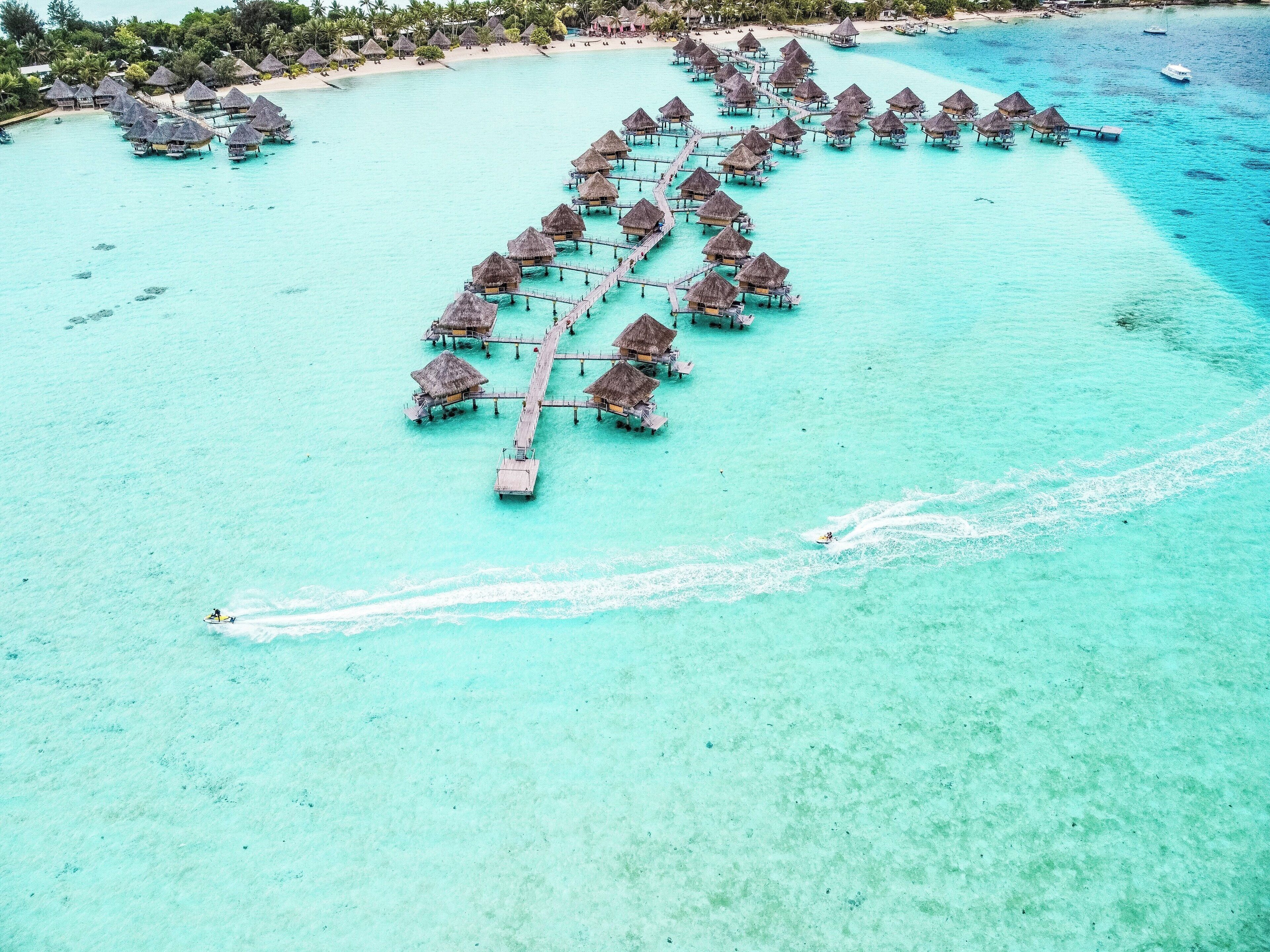Een luchtbeeld van bungalows boven het water, verbonden door looppaden over turquoise water.