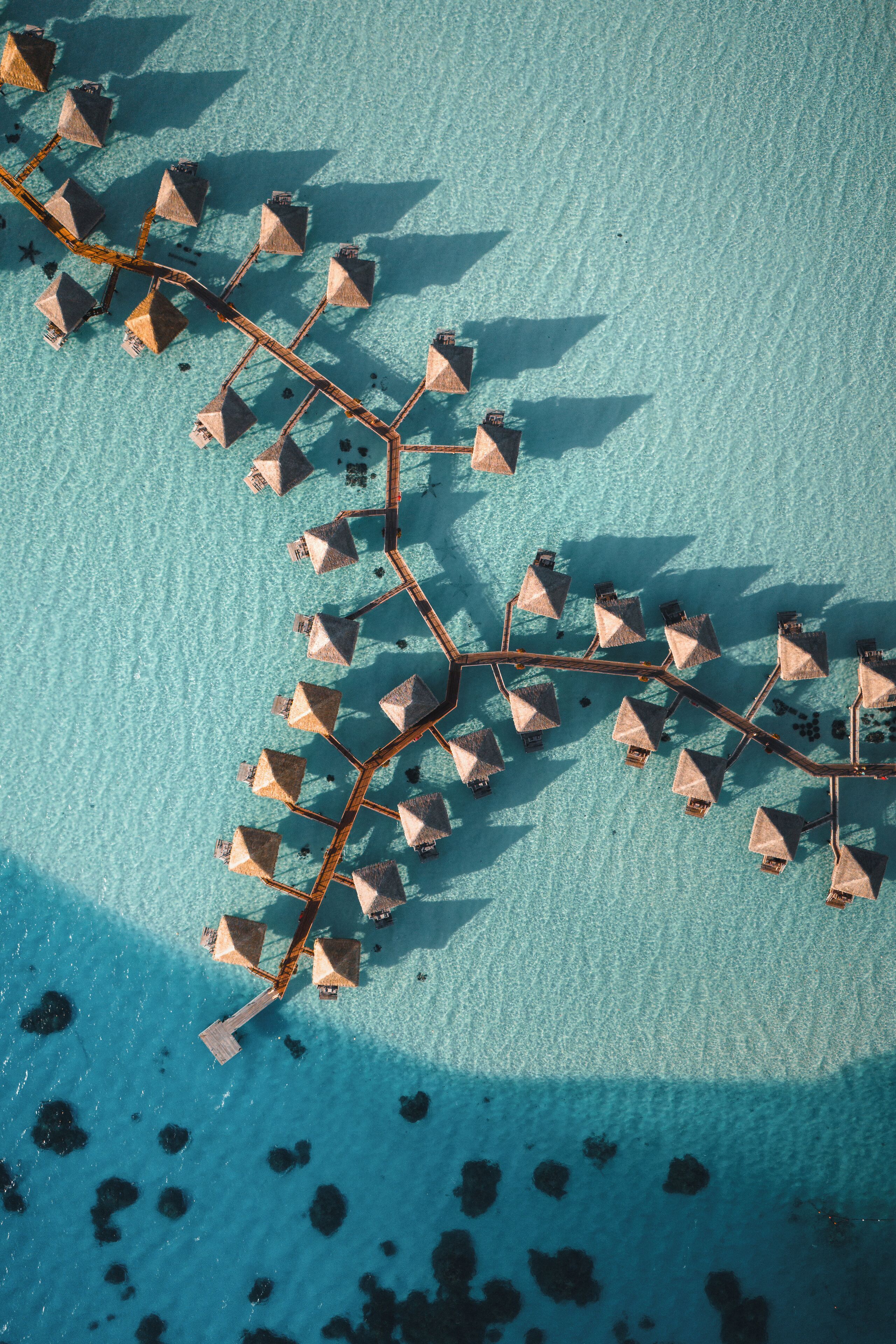 An aerial view of overwater bungalows connected by a wooden walkway.