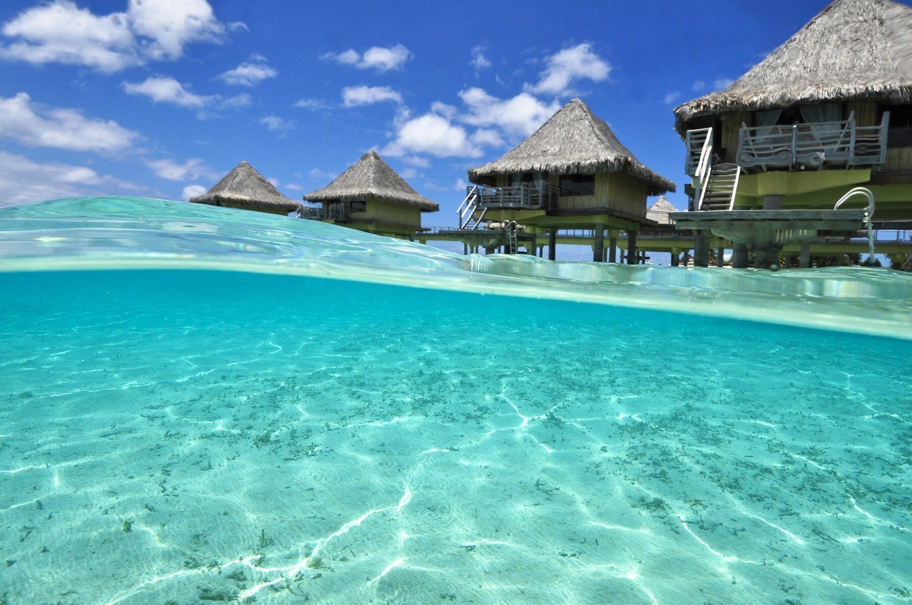 Bungalow sull'acqua con acque turchesi cristalline, tetti di paglia e una scala che conduce alla spiaggia.