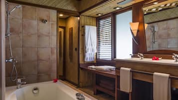 Un baño con una bañera grande, vigas de madera en el techo, ducha y tocador con espejo.