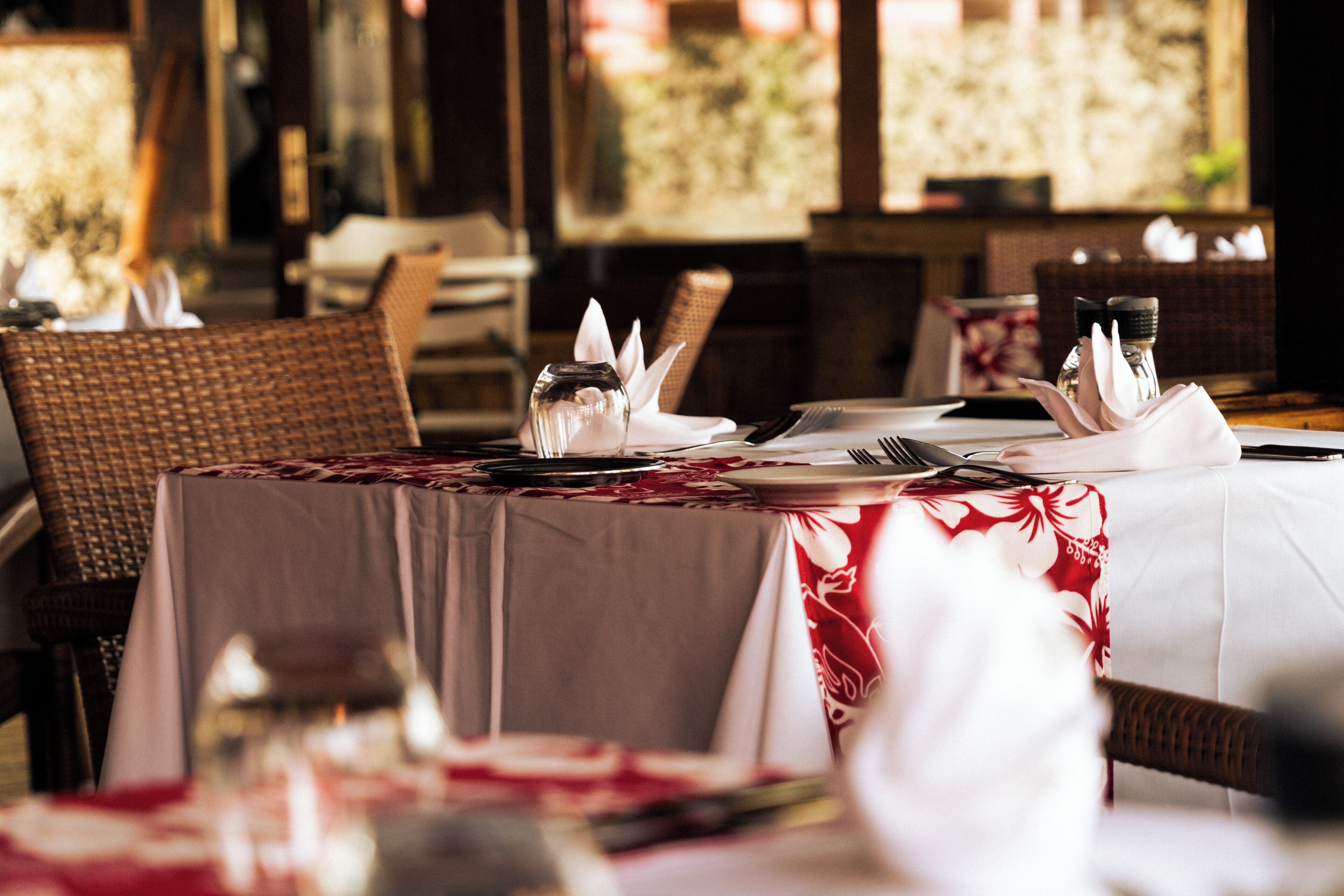 A dining area with tables set for two, featuring white napkins, cutlery, and glassware.