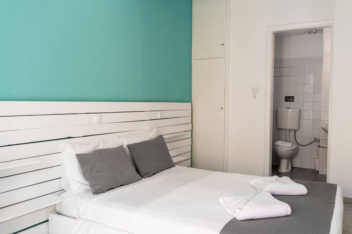 A bedroom with a bed, white headboard, grey pillows, and a grey mattress.