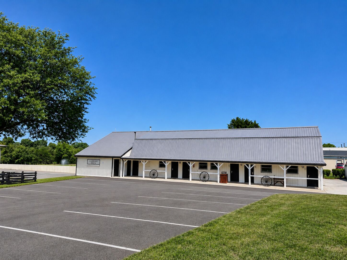 A building with a covered porch, a parking lot, and a large tree.