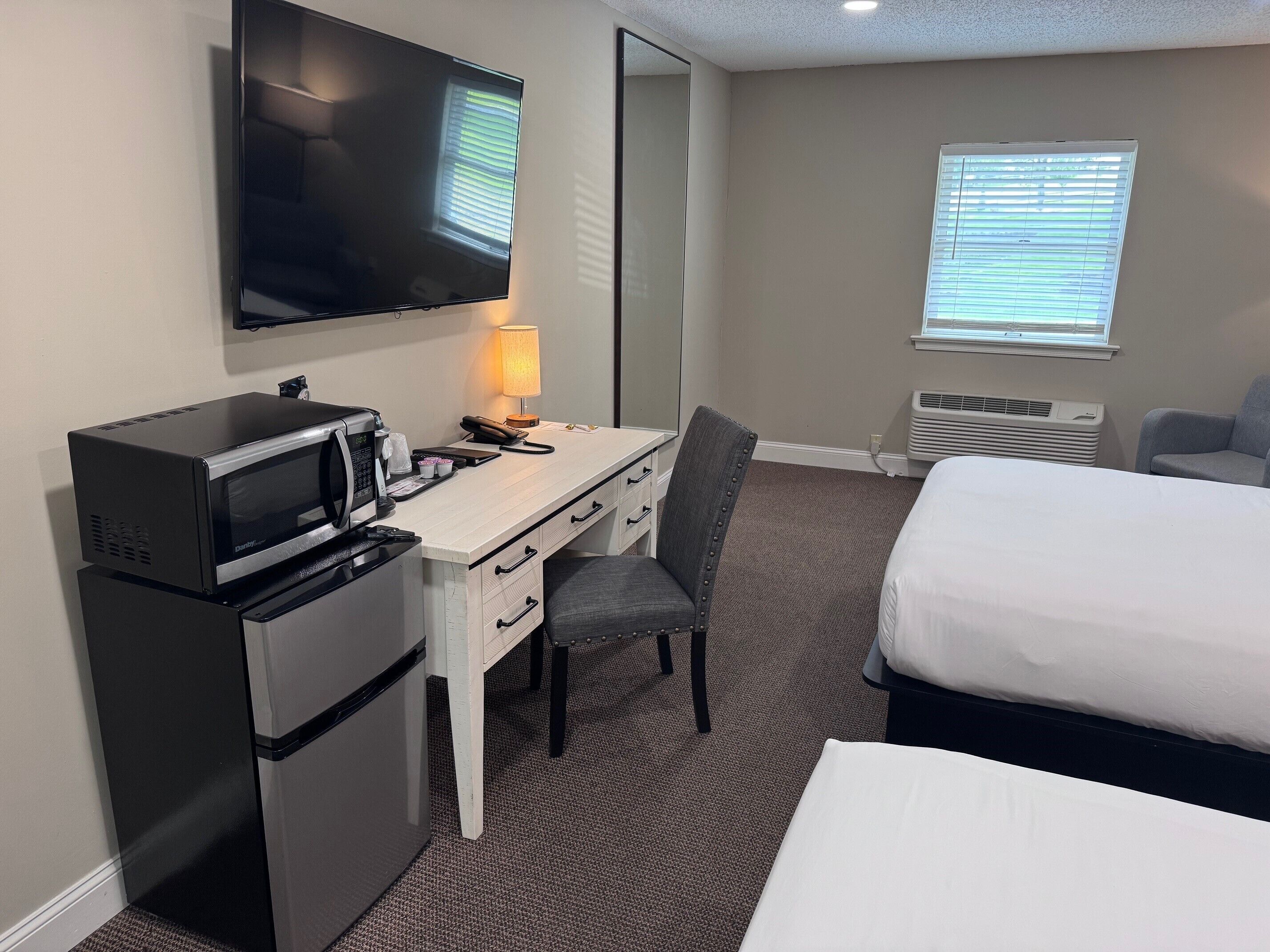 Ein Hotelzimmer mit einem Bett, einem Schreibtisch mit einer Mikrowelle, einem Stuhl, einem Fernseher, einer Lampe und einem Fenster mit Jalousien.