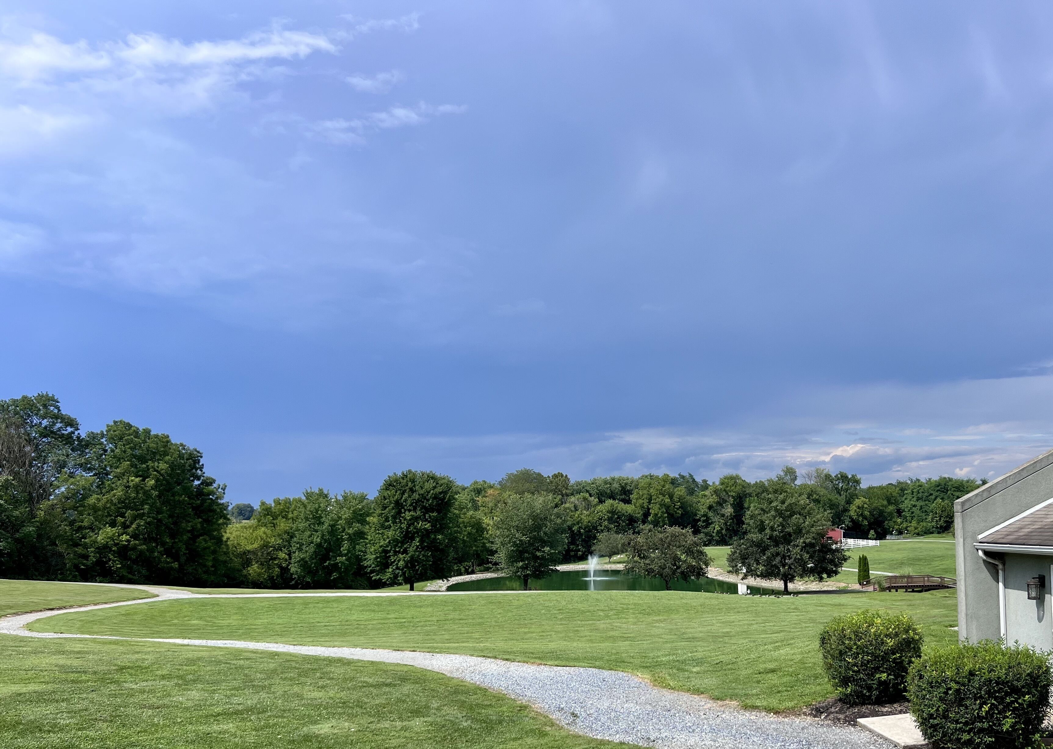 A well-maintained grassy area with a pathway leading to a pond, surrounded by trees and a building.