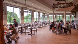 A spacious dining area with multiple tables and chairs, large windows offering views of the outdoors, and a high ceiling with hanging chandeliers. - Hersey Farm Resort  (Ronks)