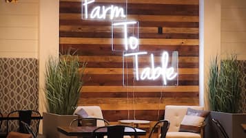 A modern interior with a neon sign reading "Farm To Table," wooden panel walls, and a seating area with tables and chairs.