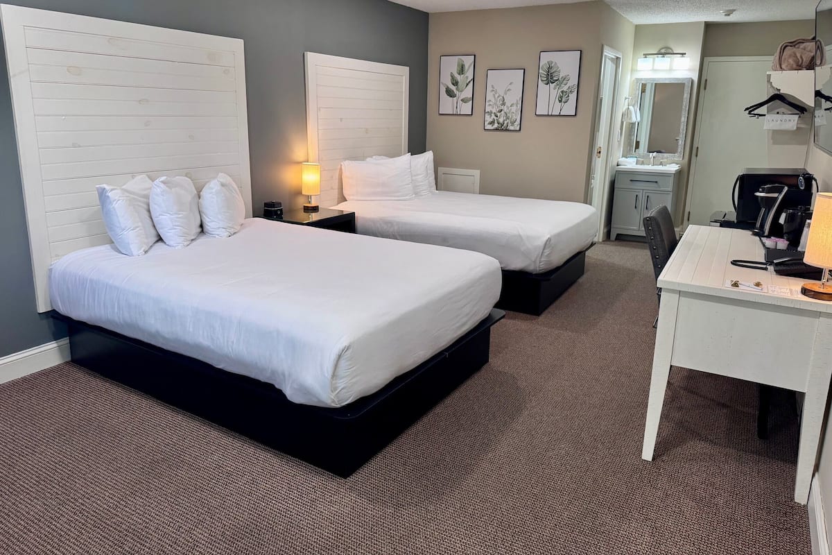 A hotel room with two beds, a desk, a mirror, and a small kitchenette.